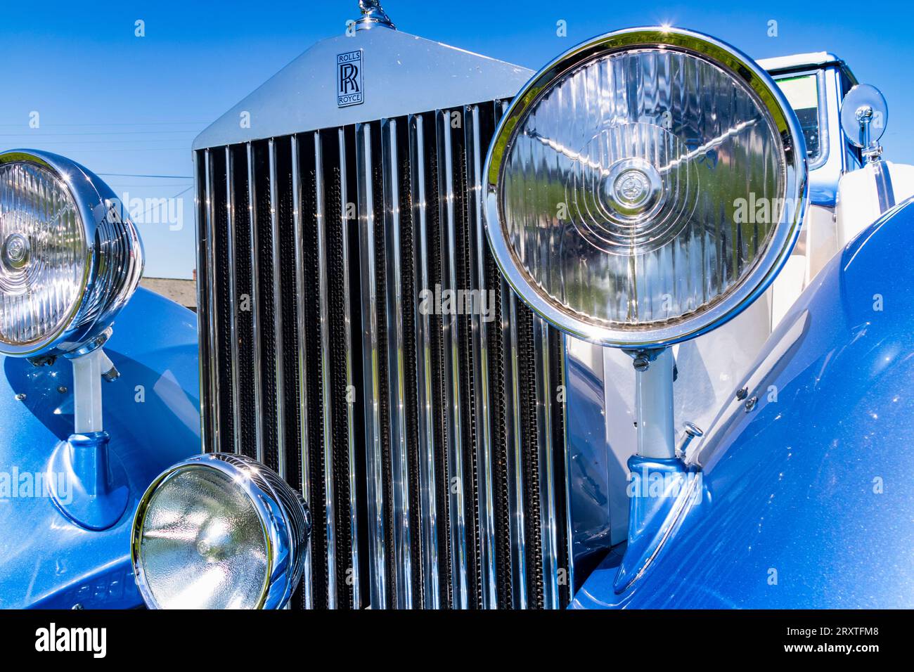 Nahaufnahme: Vorderansicht eines Vintage Rolls Royce mit verchromten Scheinwerfern, Grill und Logo vor einem blauen Himmel. Stockfoto