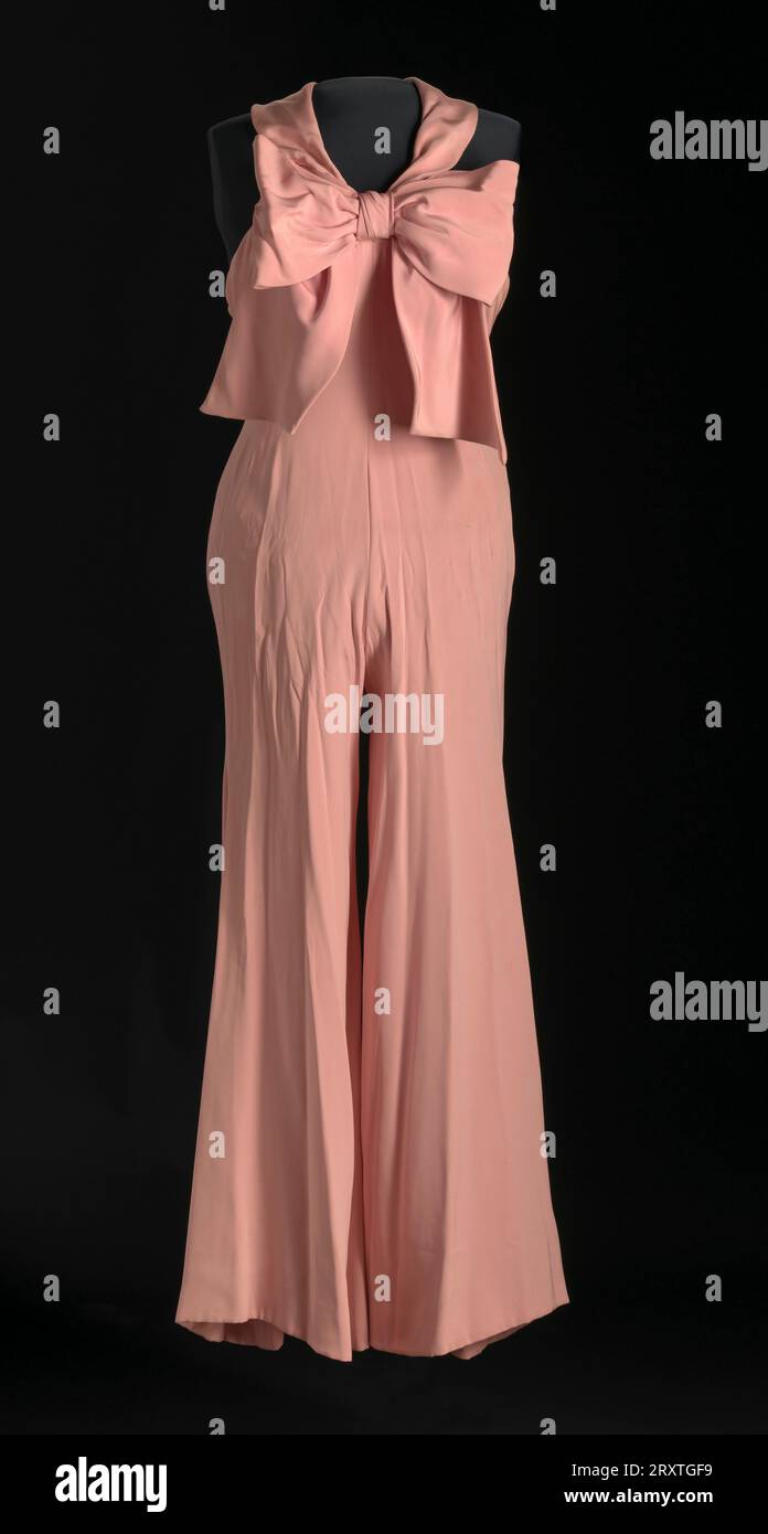 Jumpsuit von Diahann Carroll als Julia Baker in der Fernsehsendung Julia. Der Jumpsuit ist ein Neckholder mit einer großen Schleife im Vorderteil und breiten Beinen. Das Halteroberteil hat zwei (2) breite Riemen und wird am Nackenbereich mit einem Metallhaken am rechten Riemen befestigt. (Die Öse am rechten linken Riemen fehlt.) Eine übergroße Schleife mit langen Schwänzen ist vorne in der Mitte des Jumpsuits angenäht. An der Vorderseite des Jumpsuits befindet sich eine Mittelnaht, die sich an der Innenseite jedes Hosenbeins fortsetzt. Die Hose hat ein breites Bein und ist unten ausgefallen. Das Oberteil des Jumpsuits ist rückenfrei Stockfoto