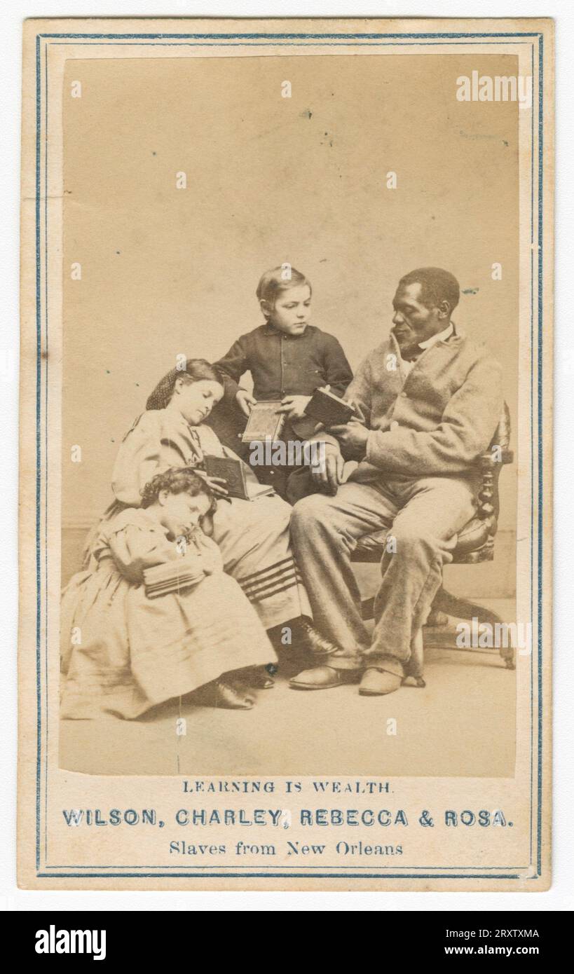 Carte de viste zeigt ein Schwarzweißfoto von drei Kindern, zwei Mädchen und einem Jungen, die um einen afroamerikanischen Mann in einem Stuhl sitzen. Alle führen Bücher. Die Bildunterschrift lautet: „Learning is Wealth“, „Wilson, Charley, Rebecca & Rosa“, „Slaves from New Orleans“. Stockfoto