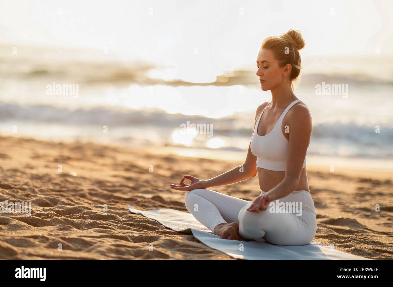 Junge europäische Frau genießen Workout, Atmungsübungen, üben Yoga in Lotusposition am Strand, freien Platz Stockfoto