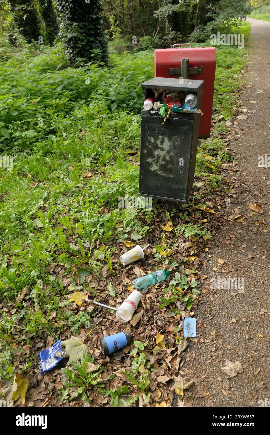 Überlaufender Metallmüll mit Müll in Form von Plastikbechern und Flaschen auf dem Boden neben einem Pfad, wie in einem öffentlichen Park in England, Großbritannien Stockfoto