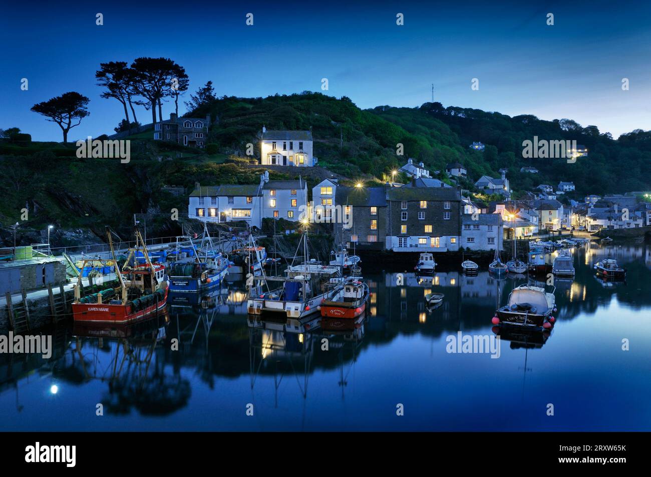 Cottages und Lichter und Fischerboote spiegeln sich im Hafen des kornischen Fischerdorfes Polperro wider, während die Abenddämmerung in die Nacht übergeht. Cornwall, England, Großbritannien Stockfoto