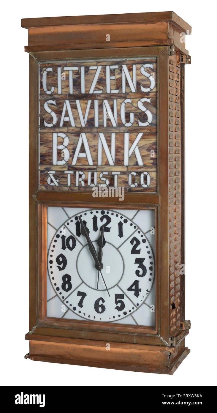 Eine große rechteckige Uhr und ein Schild (2013.208.2a). Auf der Vorder- und Rückseite der Uhr befindet sich ein Buntglasschild mit der Aufschrift „CITIZENS / SAVINGS / BANK / & TRUST CO.“ Die Uhr befindet sich unter dem Buntglasschild auf der Vorderseite der Uhr. Das Gehäuse der Uhr besteht aus Kupfermetall. Die Seiten der Uhr bestehen aus Kupfer und haben kleine, belüftungsartige Muster, die von oben nach unten verlaufen. Die Rückseite der Uhr hat eine Öffnung, die die inneren elektrischen Komponenten der Uhr freigibt. 2013.208.2b ist die Basis der Uhr. Die Basis ist aus Holz und rechteckig. Die Basis hat ein paar Gesimse A Stockfoto