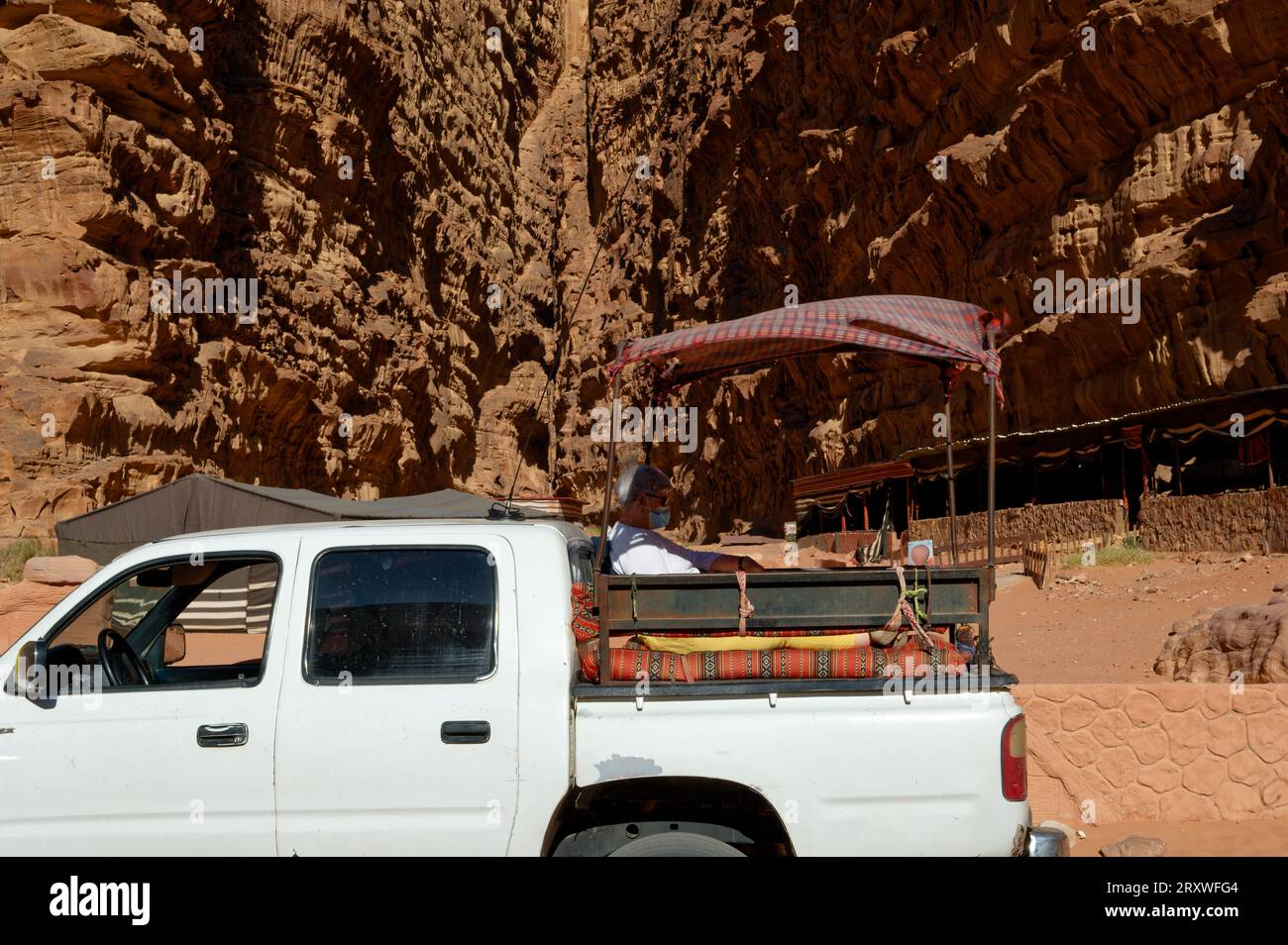 Ein Senior Adventurer, der die Pracht der Natur von einem Pickup-Truck aus betrachtet. Älterer Tourist in der Wadi Rum Wüste Stockfoto
