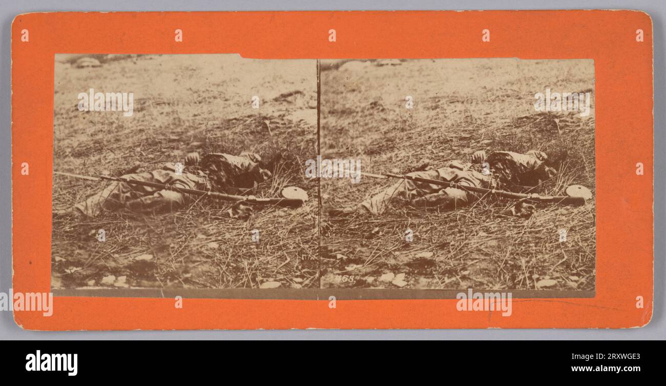 Dieser Stereograph mit Fotodruck zeigt den Leichnam eines verstorbenen konföderierten Soldaten, als er im Juli 1863 auf dem Schlachtfeld von Gettysburg, Pennsylvania, fiel. Der Mann liegt auf dem Rücken, seine Füße liegen der Kamera am nächsten. Seine Kantine liegt neben seiner linken Hand im Gras und sein Langarm mit Bajonett liegt über seinem Körper. Das Foto ist auf orangefarbenem Karton mit einem rosafarben Ton auf der Rückseite angebracht, der leer ist. Stockfoto