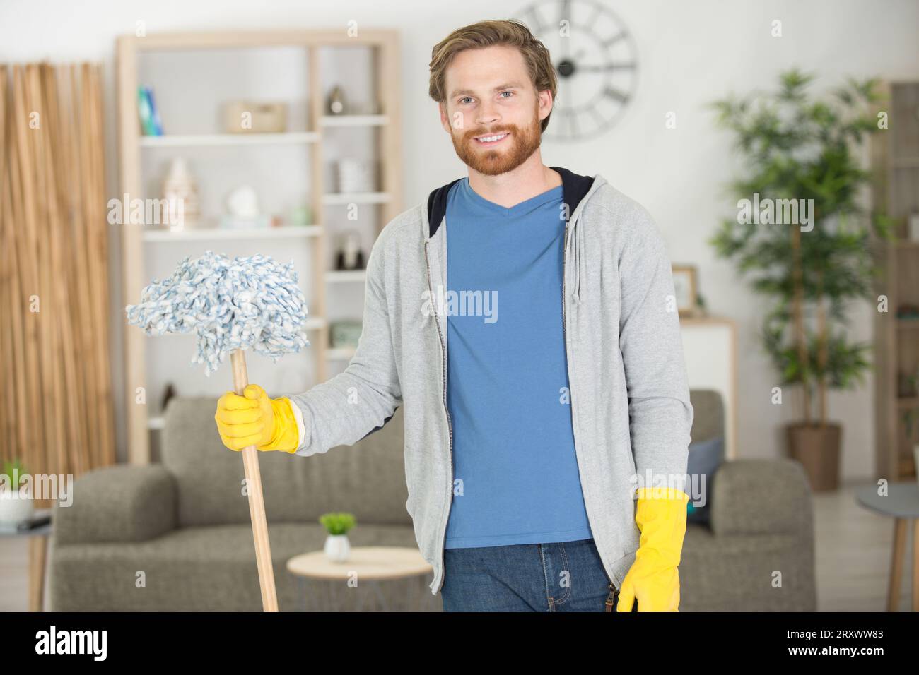 Männlicher Reiniger mit Mopp lächelt vor der Kamera Stockfoto