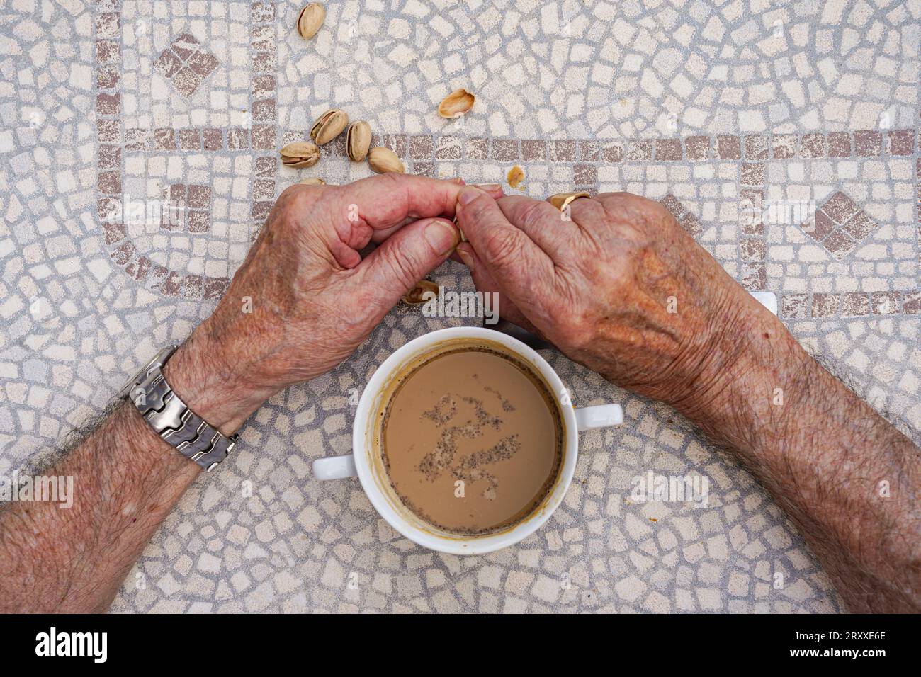 Älterer Mann hat die Hand zerknittert, einen Kaffee getrunken und Pistazien gegessen. Aktives Alter beim Snack. Luftaufnahme. Stockfoto