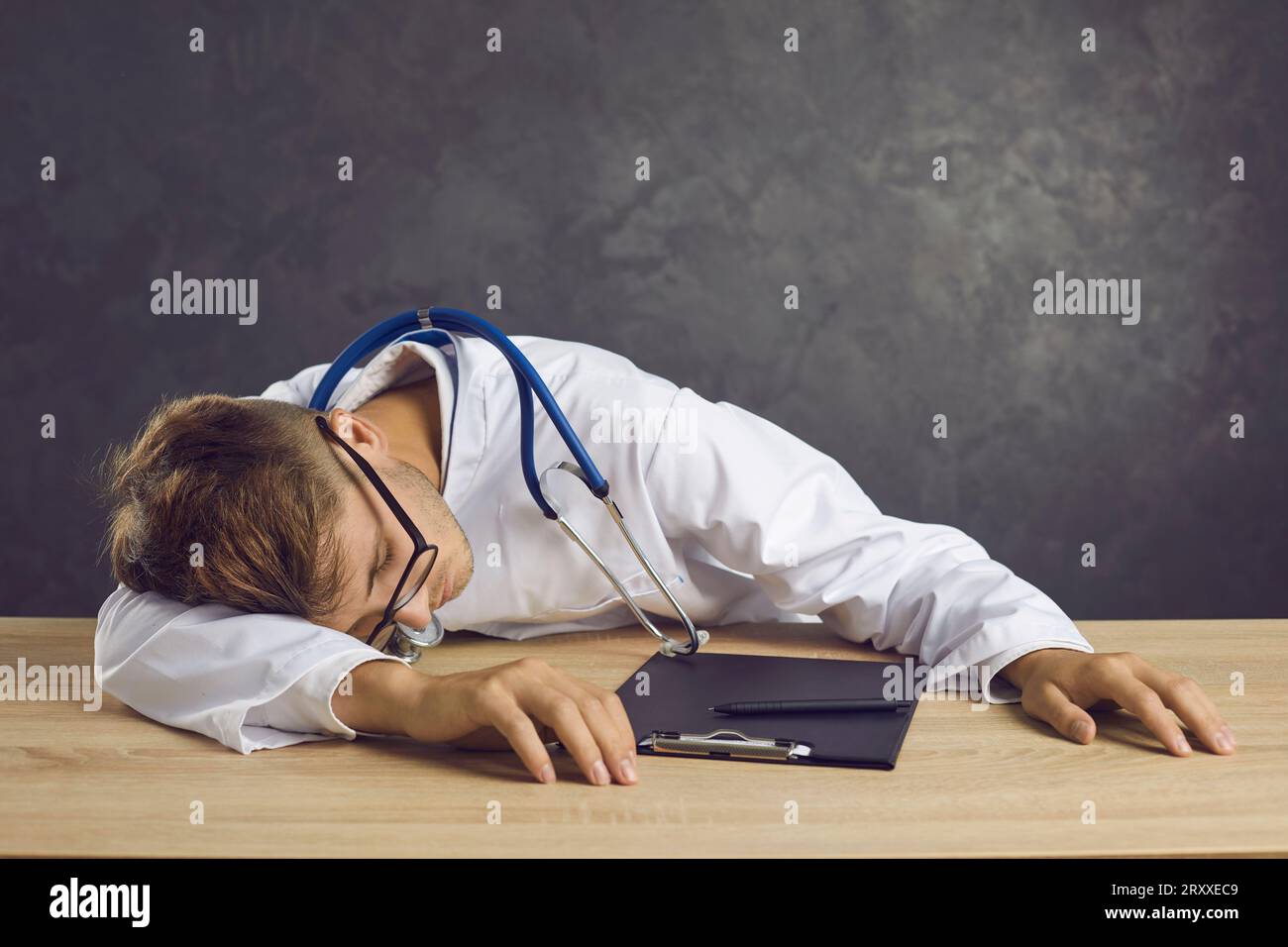 Studio-Porträt eines müden und erschöpften jungen Mediziners, der am Tisch schläft. Stockfoto