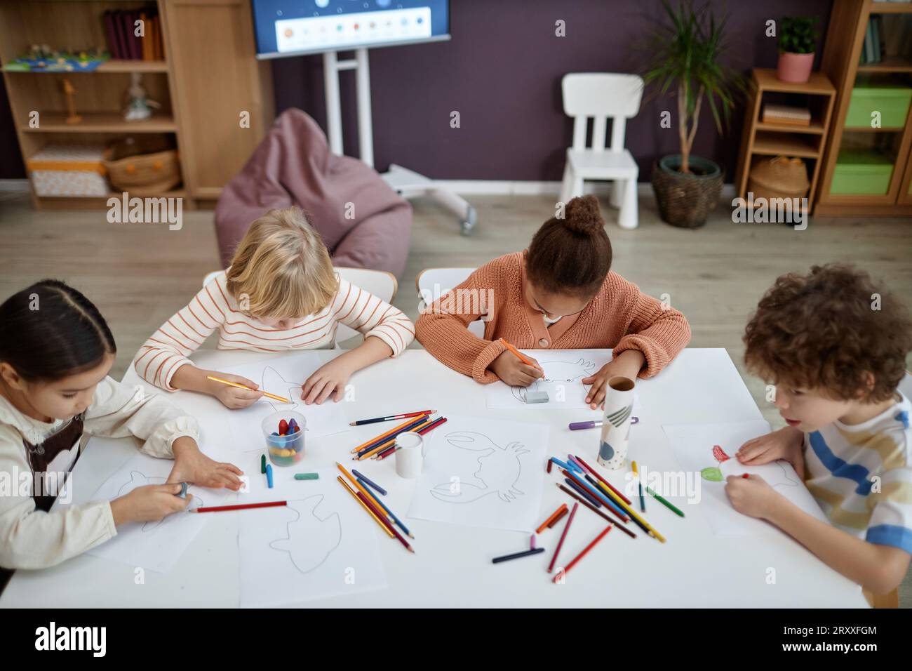 Blick von oben auf eine multiethnische Gruppe von Kindern, die Kunst und Kunsthandwerk machen, die im Vorschulunterricht am Tisch sitzen, Kopierraum Stockfoto