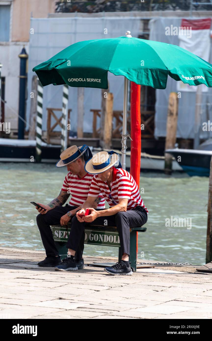 Ein paar Gondoliere verbringen Zeit mit ihren Mobiltelefonen, während sie auf Kunden an einer der Gondelstationen am Canal Grande in warten Stockfoto