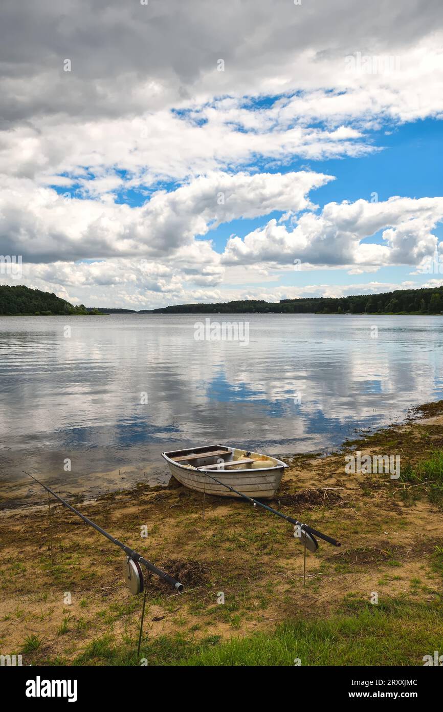 Tagsüber Urlaubslandschaft am Wasser. Boot am Ufer des Sees und Wolken spiegeln sich im Wasser. Fotos am Chancza-See, Polen. Stockfoto