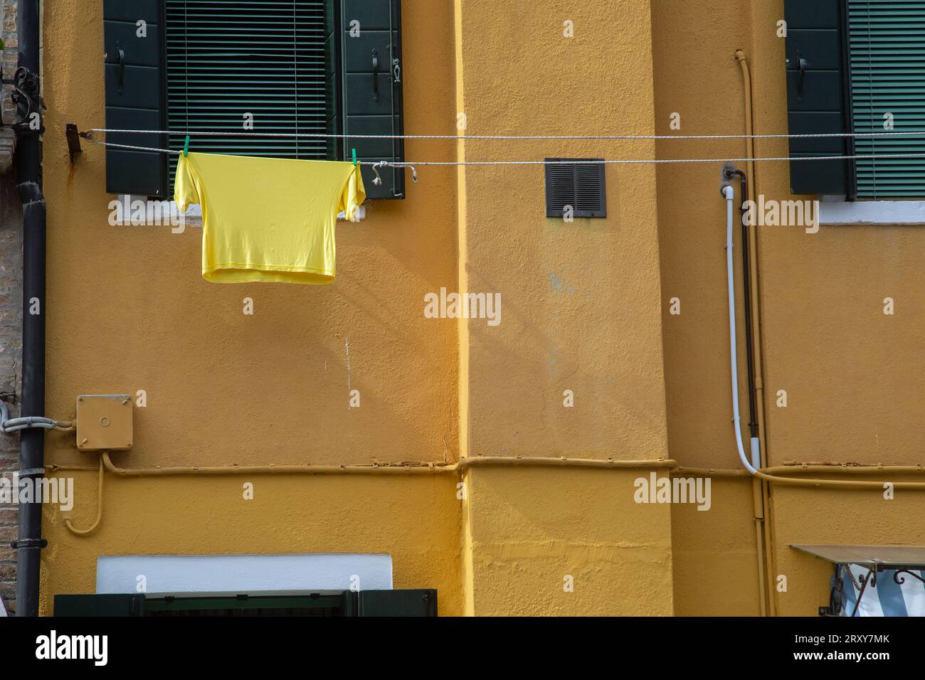 Ein gelbes T-Shirt auf einer Wäscheleine vor einer gelben ockerfarbenen Wand in Burano Stockfoto