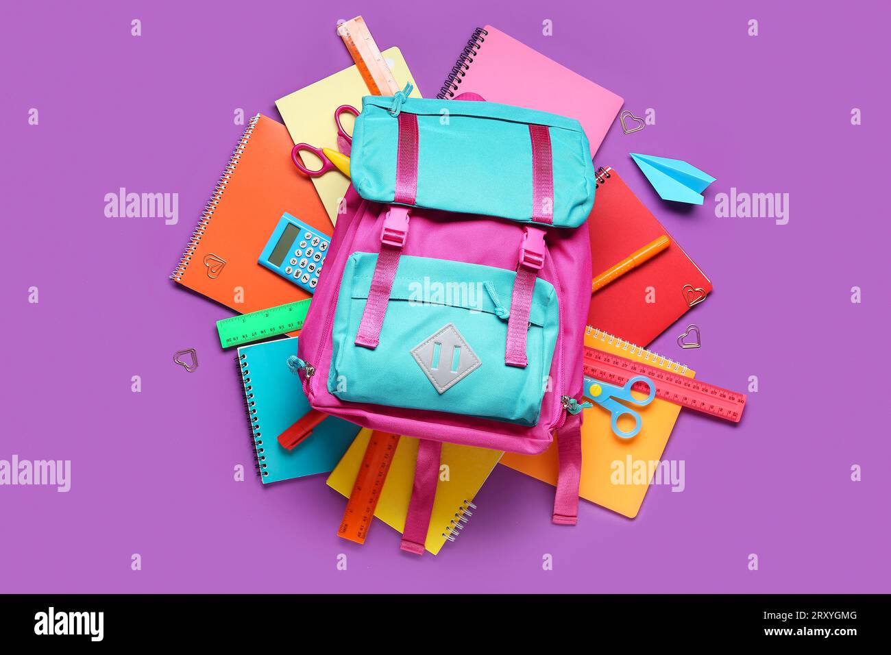 Stylischer Schulrucksack und verschiedene Schreibwaren auf violettem Hintergrund Stockfoto