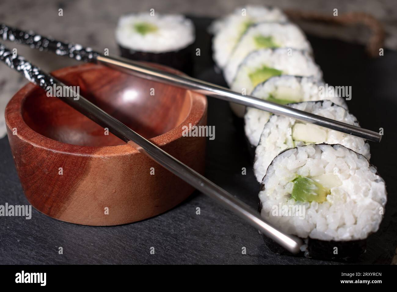 Hausgemachtes vegetarisches Sushi-Gericht mit Seetang, Reis, Gurke, Avocado und veganem Käse. Daneben ein Holzbehälter für Sojasauce und wiederverwendbare Meta Stockfoto