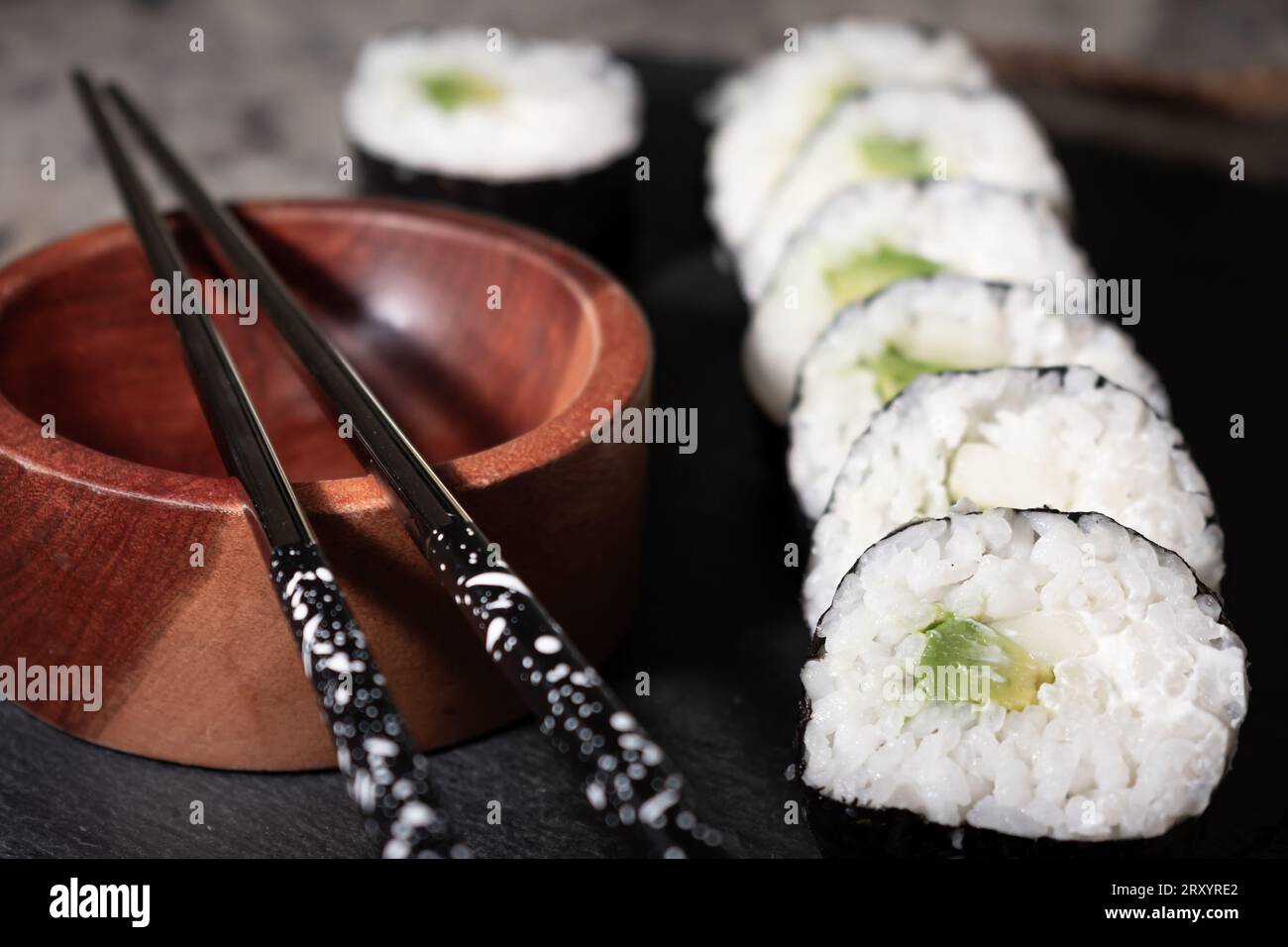 Hausgemachtes vegetarisches Sushi-Gericht mit Seetang, Reis, Gurke, Avocado und veganem Käse. Daneben ein Holzbehälter für Sojasauce und wiederverwendbare Meta Stockfoto