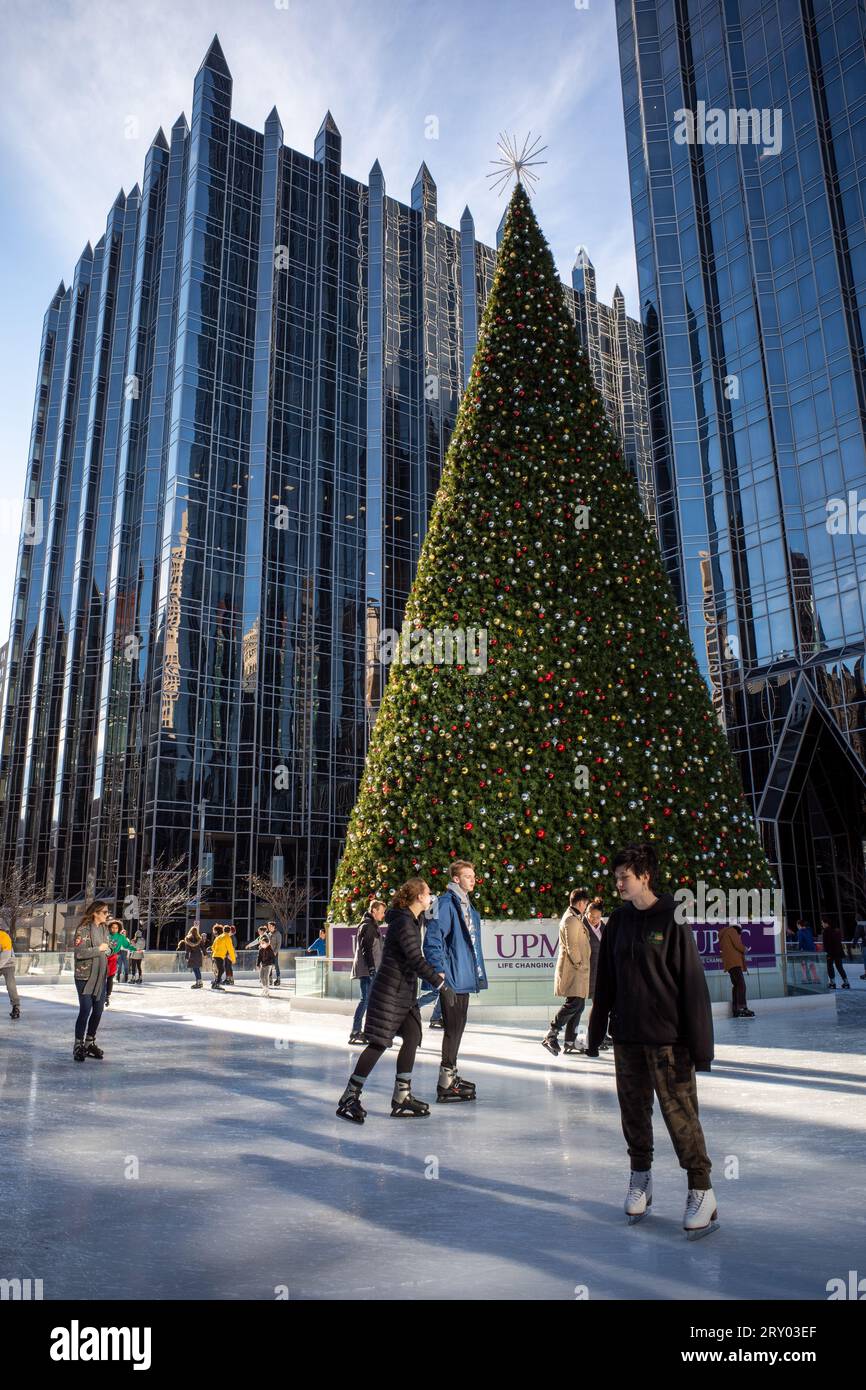 Gleiten Sie anmutig über das Eis, umrahmt vom majestätischen Weihnachtsbaum am PPG Place in der Innenstadt von Pittsburgh, in der Wärme eines sonnigen Wintertages. Stockfoto