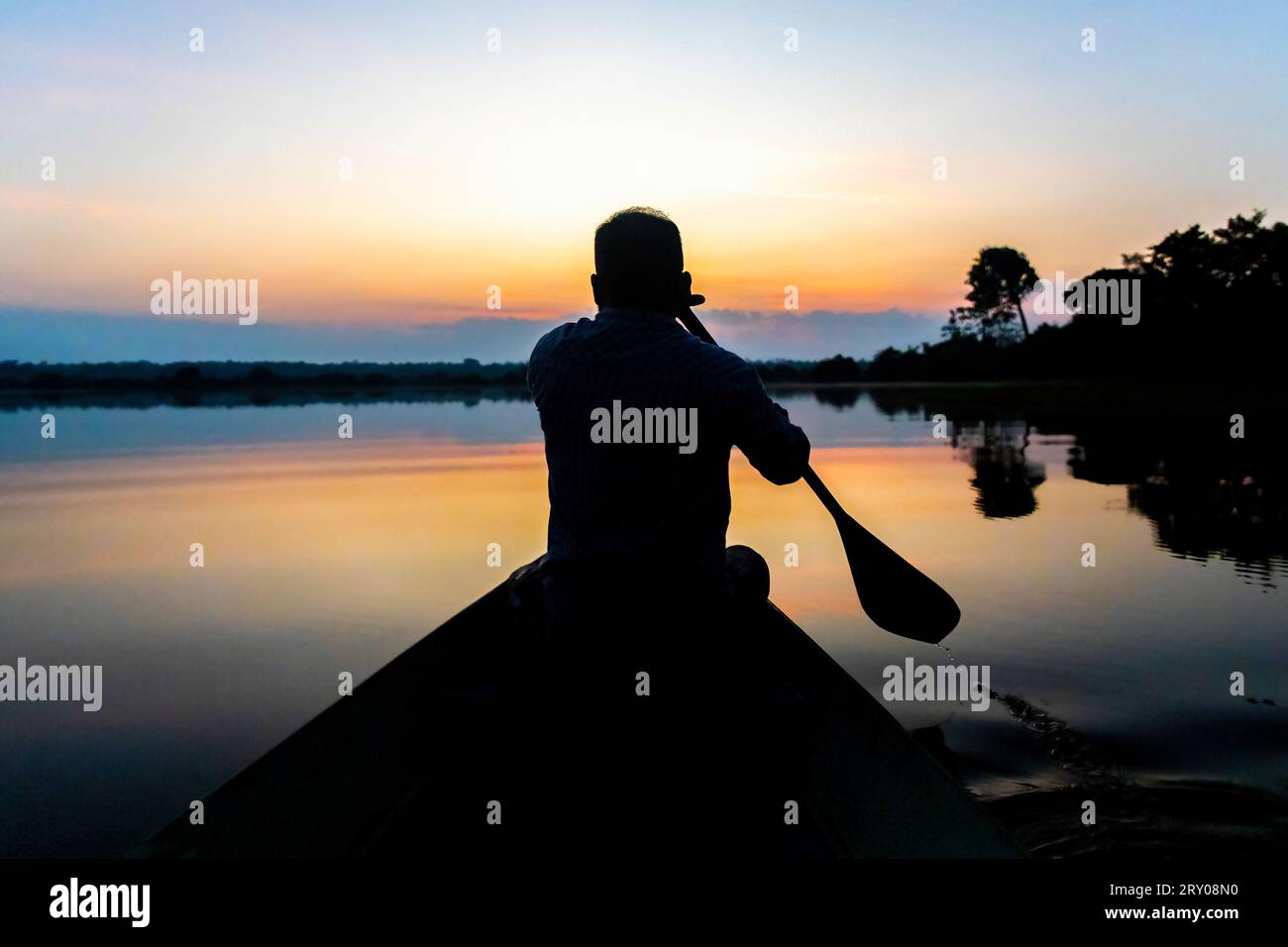 Silhouette eines einheimischen Mannes, der bei Sonnenuntergang im ruhigen Wasser Kanu paddelt Stockfoto