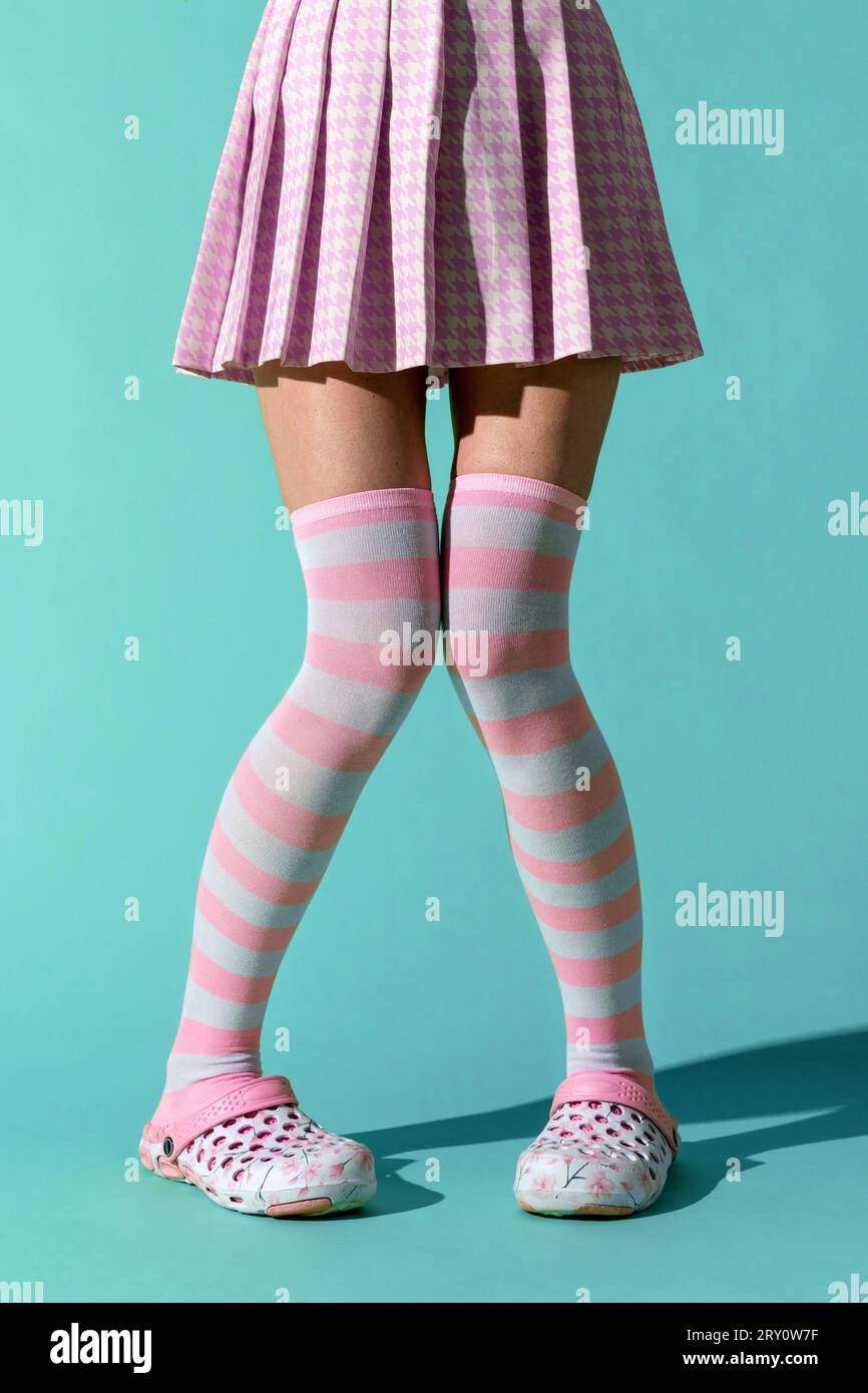 Anonymes junges Mädchen, das mit Schatten auf dem Boden steht und die Knie mit den Füßen auseinander hält und ein lustiges rosafarbenes Outfit aus Rock-Socken trägt Stockfoto