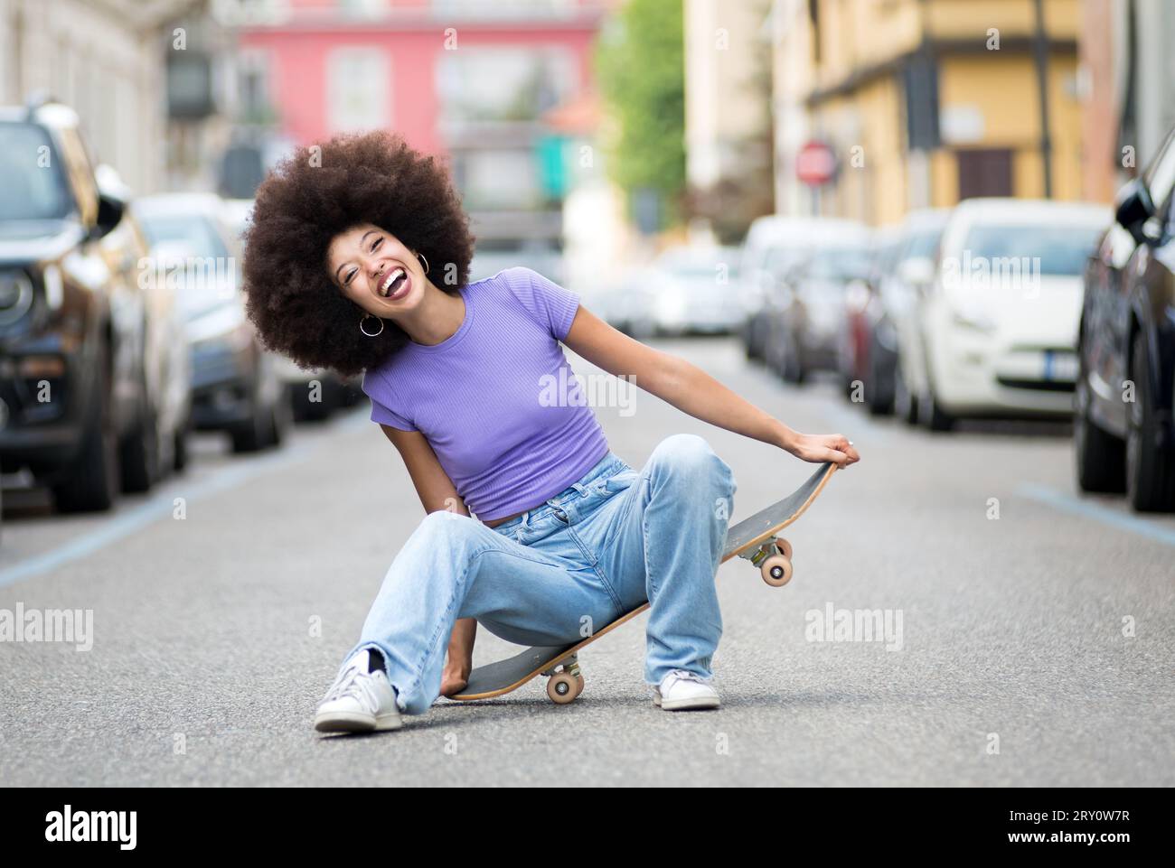 Ein voller Körper von fröhlichen jungen afroamerikanischen Skaterinnen in lässiger Kleidung, die Spaß auf dem Skateboard auf der Straße haben Stockfoto