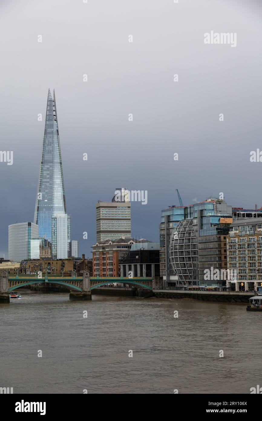 Vertikale Ausrichtung der Skyline von London City einschließlich Shard, London Bridge und Themse im Vordergrund. Keine Personen. Dramatischer Himmel Stockfoto