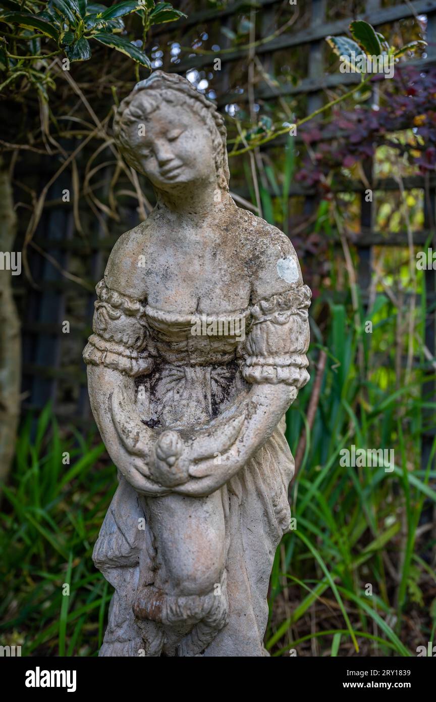 Alte Statue einer Frau, die einen Vogel mit geschlossenen Augen hält, in einem Garten steht, vertikale Aufnahme Stockfoto