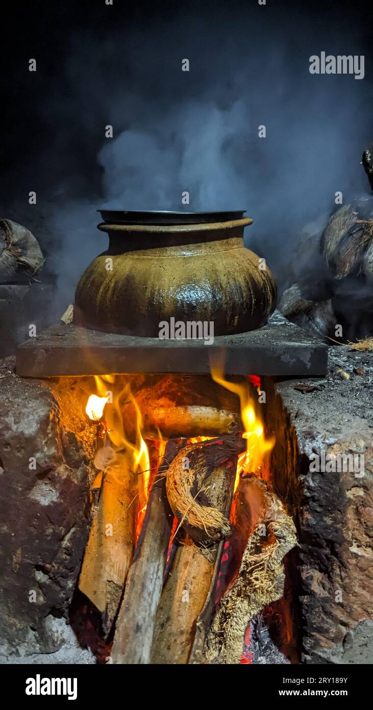 Ein brauner Wasserkocher mit Speisen, die unter dem Feuer in einem alten traditionellen Ofen mit Brennholz gekocht und geraucht werden Stockfoto
