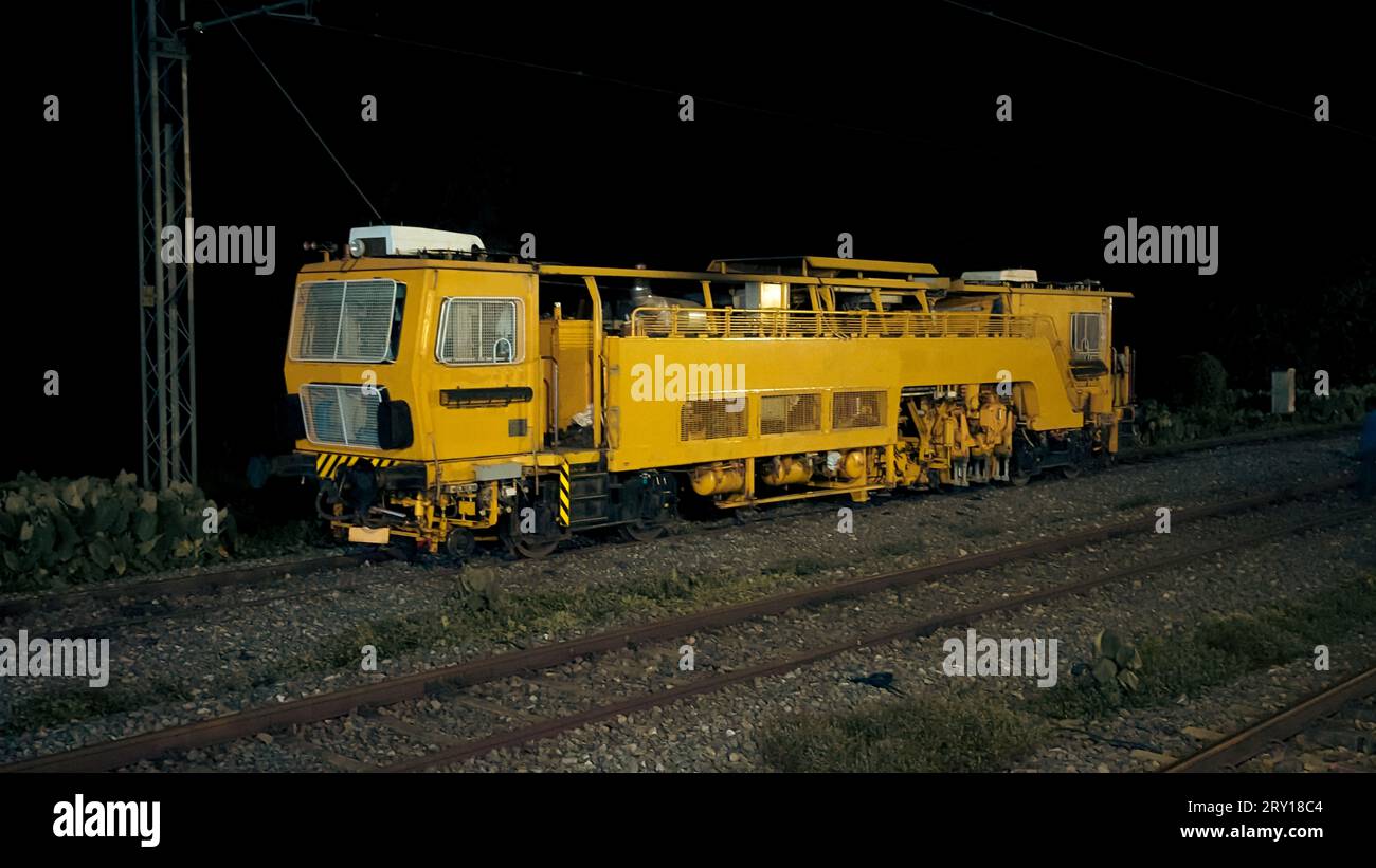 Ein alter alter gelber Lokomotiven-Dieselmotor eines Zuges auf dem Gleis in der Nähe eines Bahnhofs bei Nacht Stockfoto