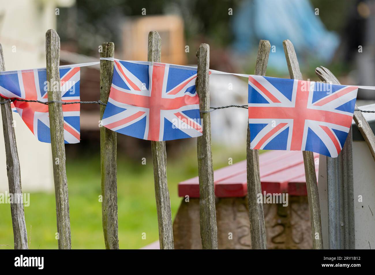 Union Jack, der auf einer Zaunreihe hagelt, viele Fahnen in Reihe auf einer Schnur, vor dem Garten VE Tagesdekorationen in Großbritannien, Stockfoto