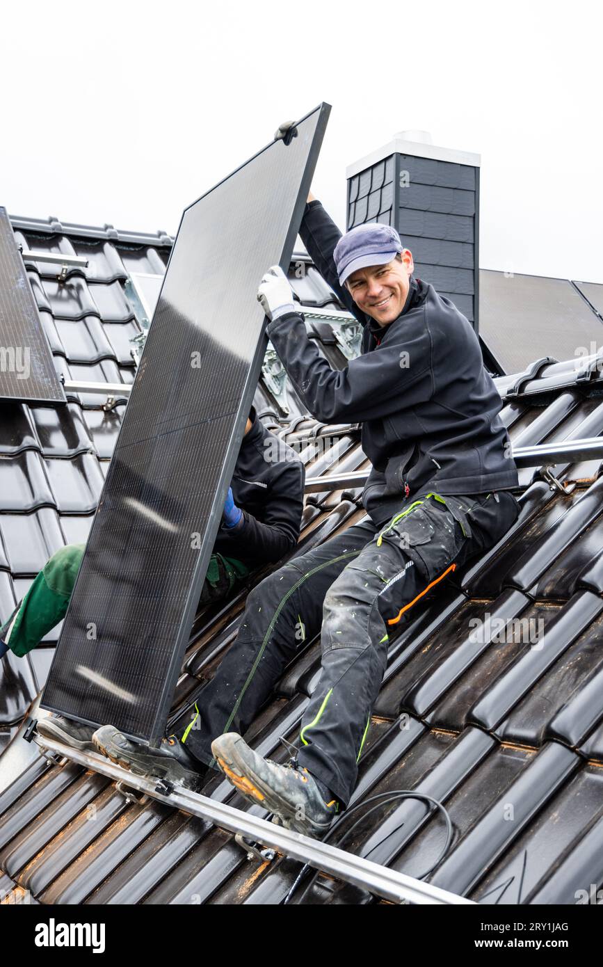 Lächelnder Techniker bei der Installation eines Solarmoduls auf dem Dach eines Hauses Stockfoto