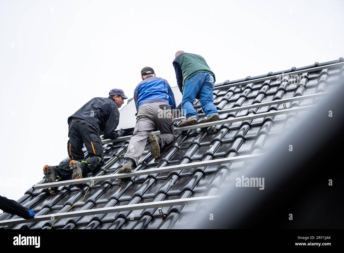 Team von Technikern, die auf dem Montagegestell für Solarmodule auf dem Dach eines Hauses stehen Stockfoto
