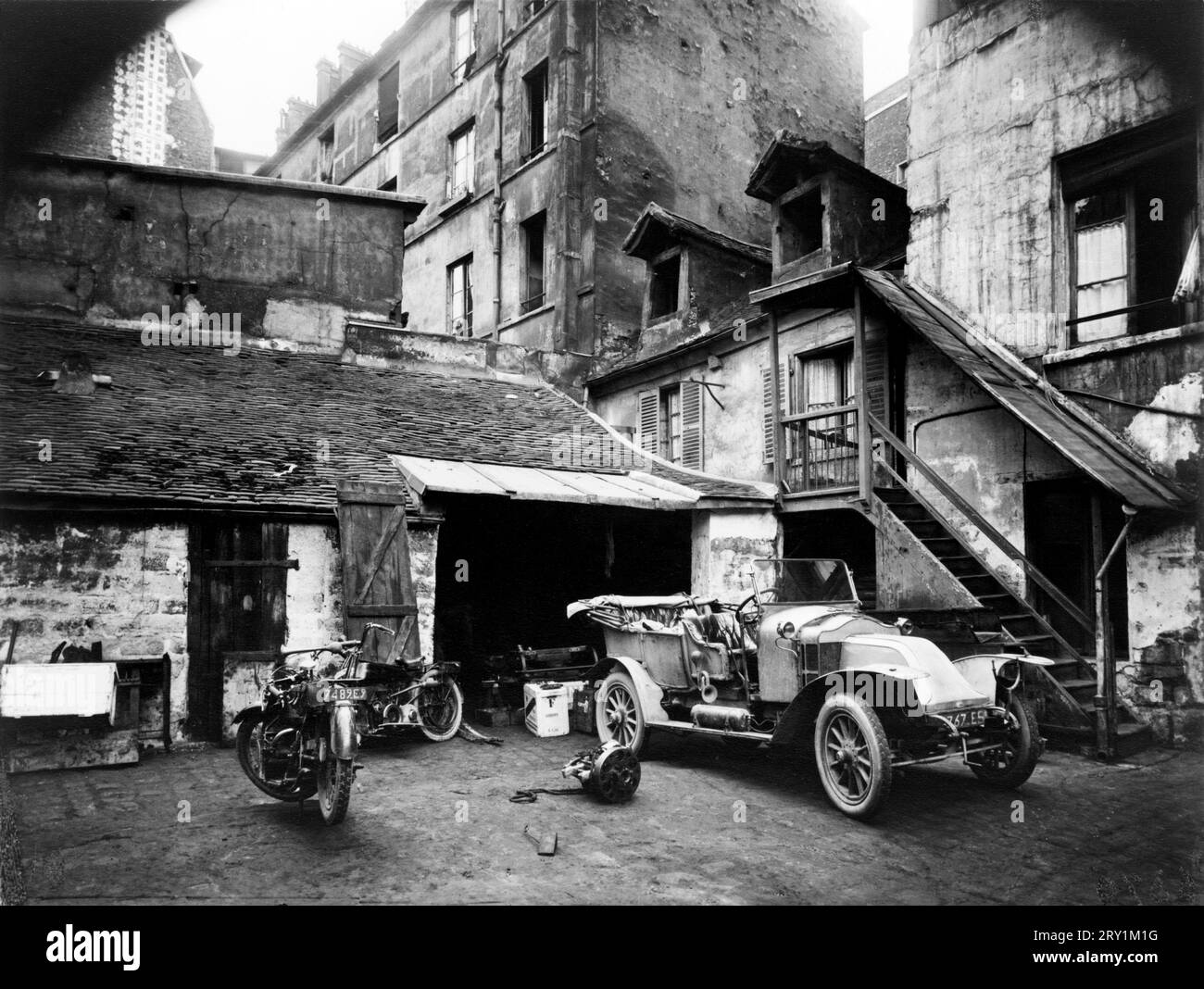 Eugène Atget: Cour, Rue de Valence, Paris, CA. 1920 Eugène Atget: cour, Rue de Valence, undatierte Fotografie, ca. 1920 Automobil und zwei Motorräder vor der Garage im Innenhof, 5e Arrondissement, Paris, Frankreich Stockfoto