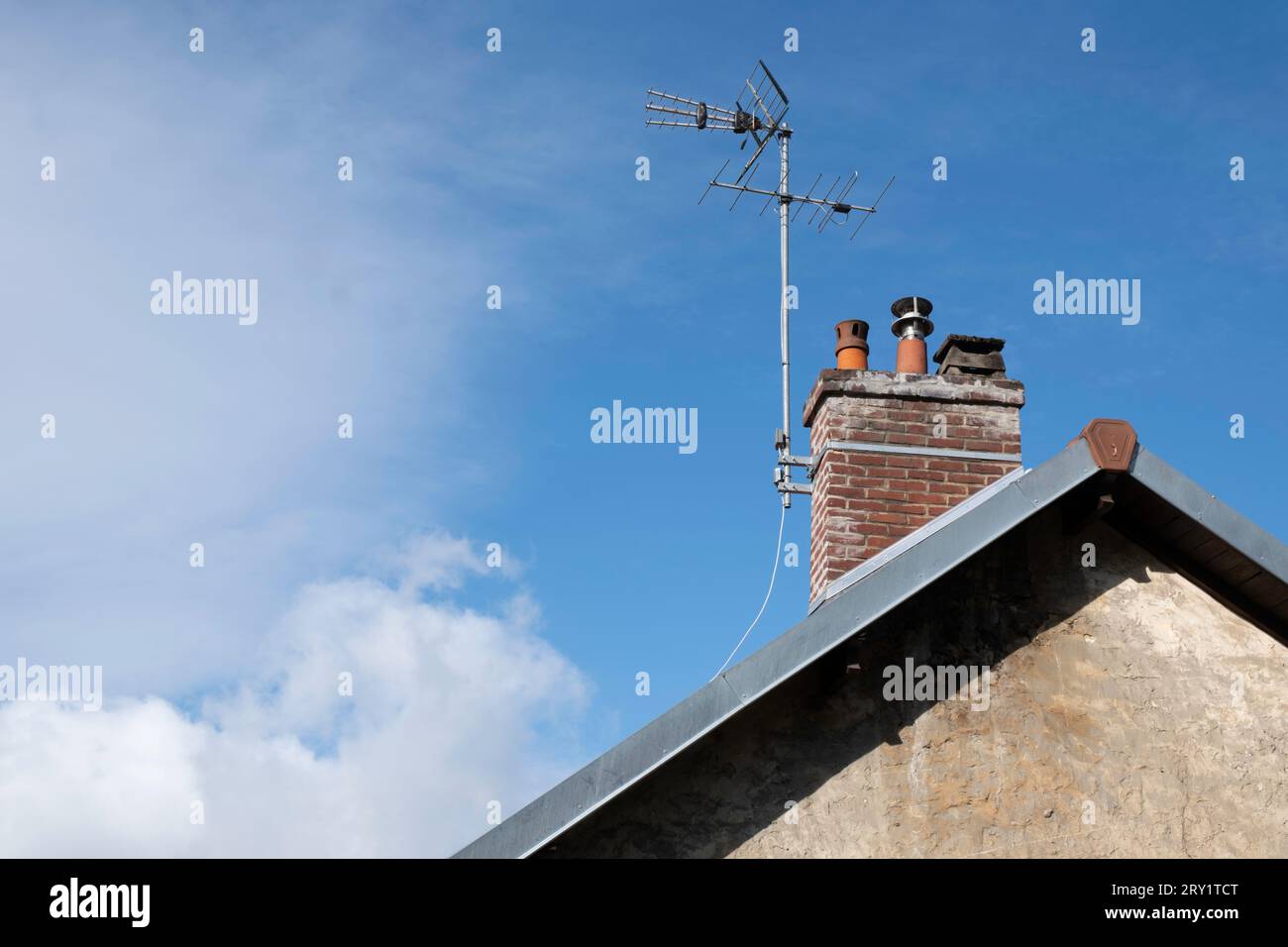 Fernsehantenne am gemauerten Kamin auf einem Hausdach mit Kalksteinwand. Blauer Himmel mit Wolken. Kopierbereich Stockfoto