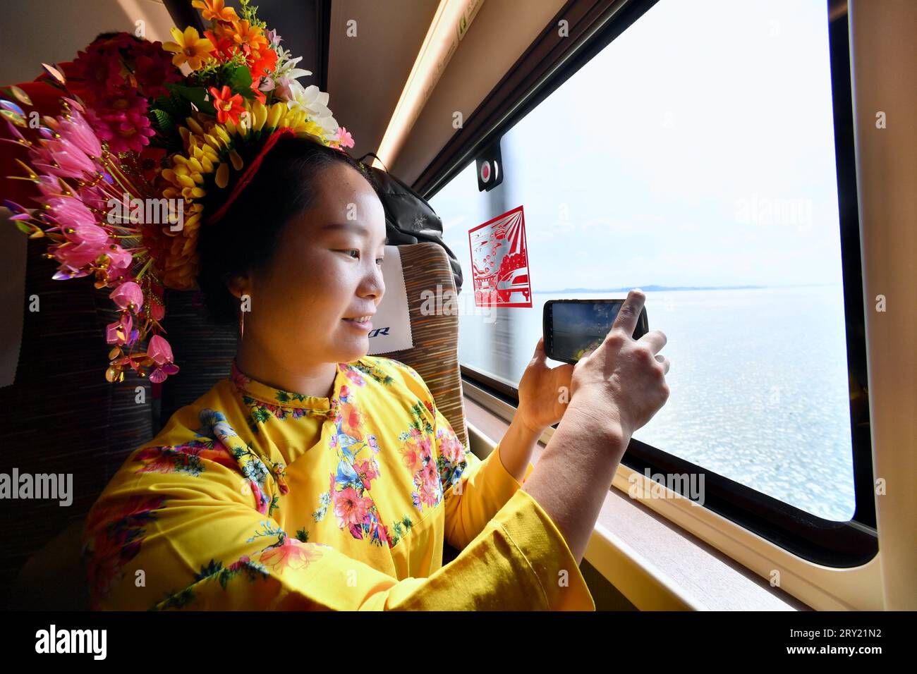 FUZHOU, 28. September 2023 (Xinhua) -- Ein Passagier, der an Bord des Fuxing-Hochgeschwindigkeitszuges G9801 mit der Fuzhou-Xiamen-Zhangzhou-Hochgeschwindigkeitsbahn reist, macht Fotos von der Landschaft vor dem Zugfenster in der südöstlichen chinesischen Provinz Fujian, 28. September 2023. Chinas schnellste Hochgeschwindigkeitsstrecke für den Seeverkehr nahm am Donnerstag den Betrieb auf, wobei die Züge mit einer Höchstgeschwindigkeit von 350 km/h entlang der Westküste der Straße von Taiwan verkehrten. Ein Fuxing-Hochgeschwindigkeitszug G9801 fuhr um 9:15 Uhr von Fuzhou, der Hauptstadt der südöstlichen chinesischen Provinz Fujian, ab und feierte die Eröffnung des 277 km langen Fuzhou-Xiamen-Zha Stockfoto