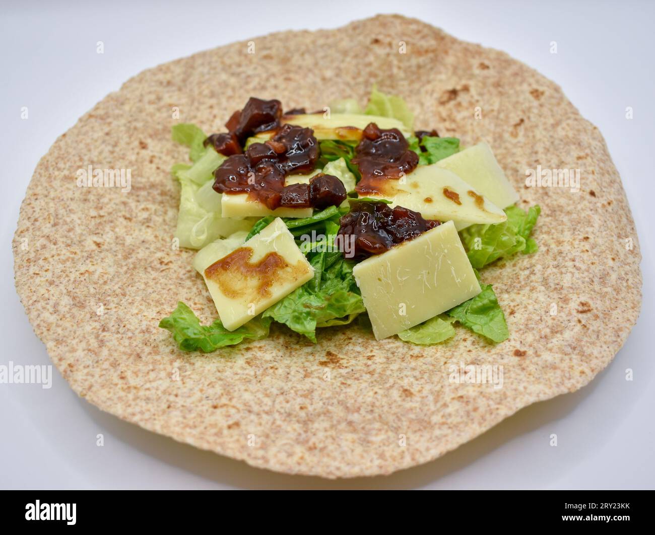 Eine Vollkorn-Tortilla-Wrap zum Mittagessen mit Cheddar-Käse, eingelegtem Chutney und geschnittenem Salat. Stockfoto