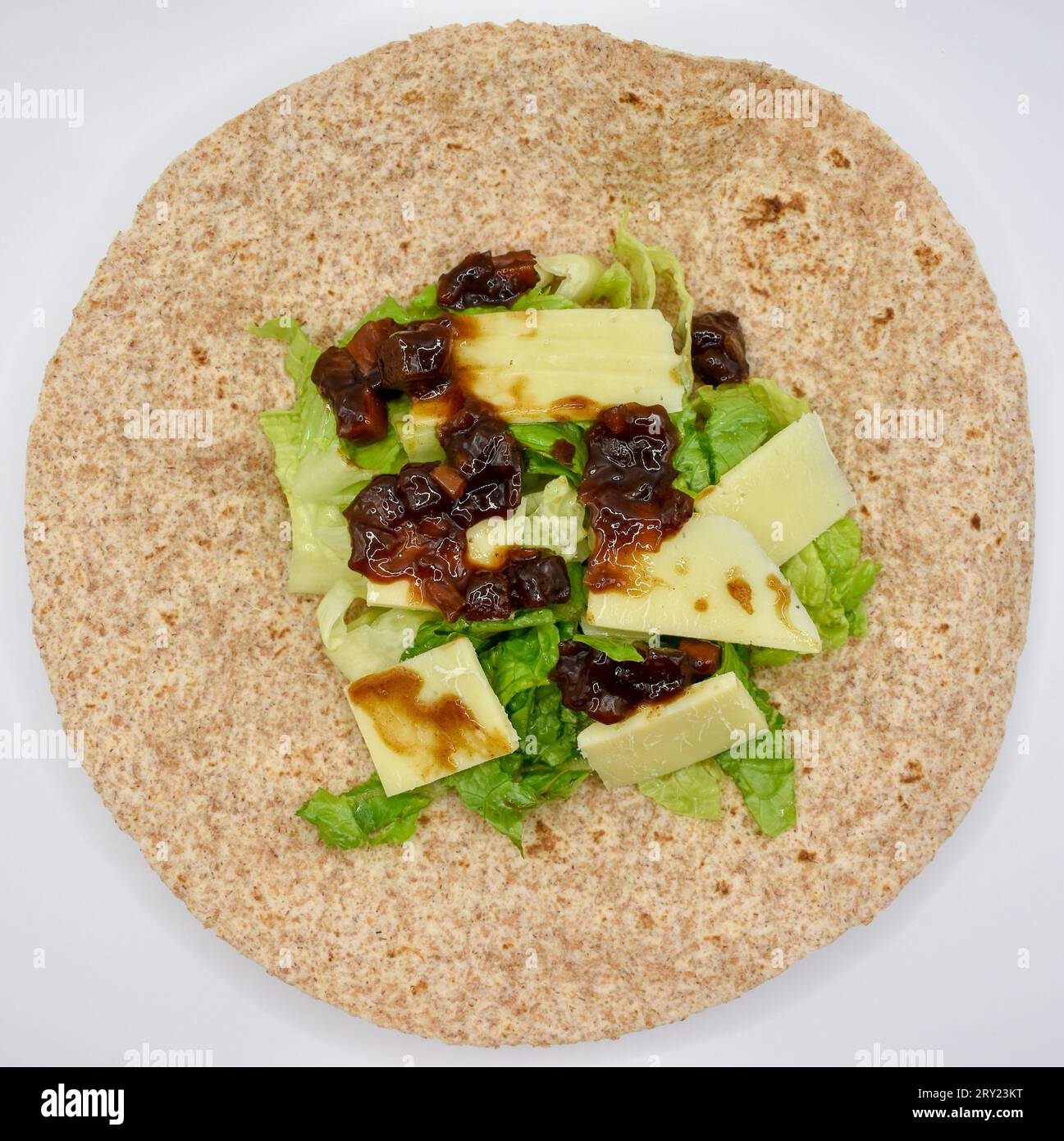 Eine Vollkorn-Tortilla-Wrap zum Mittagessen mit Cheddar-Käse, eingelegtem Chutney und geschnittenem Salat. Stockfoto