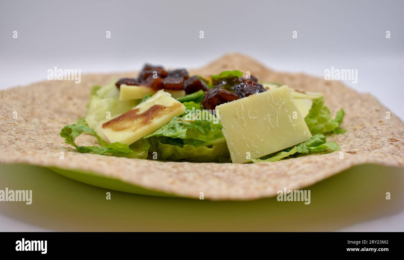 Eine Vollkorn-Tortilla-Wrap zum Mittagessen mit Cheddar-Käse, eingelegtem Chutney und geschnittenem Salat. Stockfoto