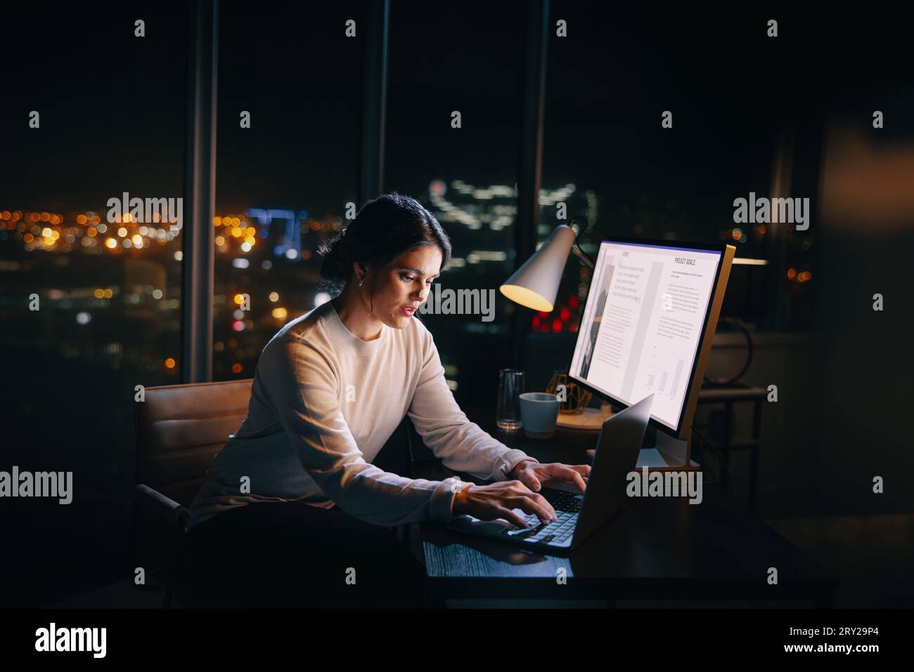 Eine engagierte Geschäftsfrau arbeitet spät und schreibt auf ihrem Laptop an ihrem Schreibtisch. Unternehmerin, die spät arbeitet, sich auf Treffen konzentriert und entschlossen ist Stockfoto