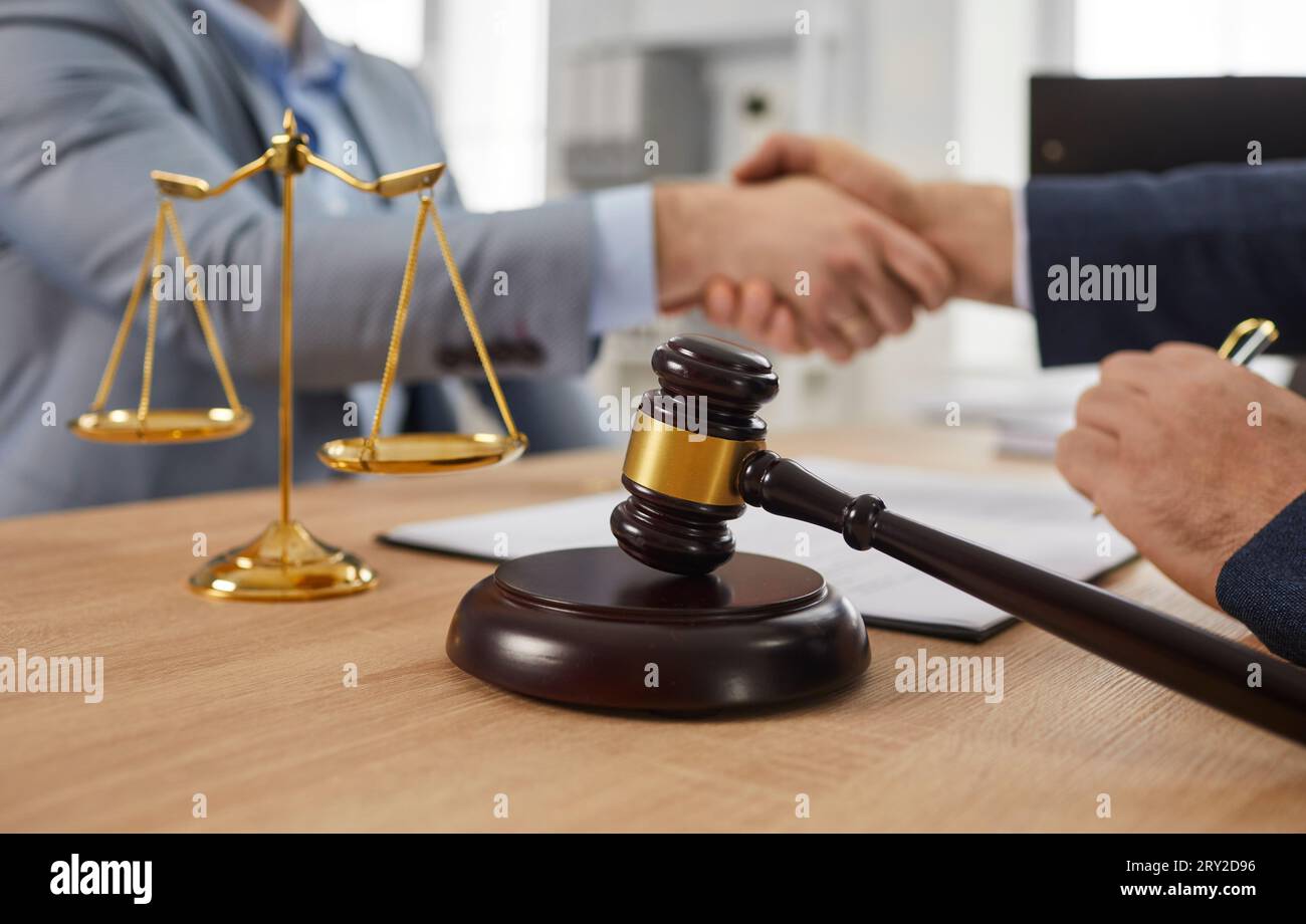 Rechtsanwalt, der an seinem Arbeitsplatz arbeitet und mit einem Mandanten im Büro auf einem Holztisch die Hand schüttelt. Stockfoto