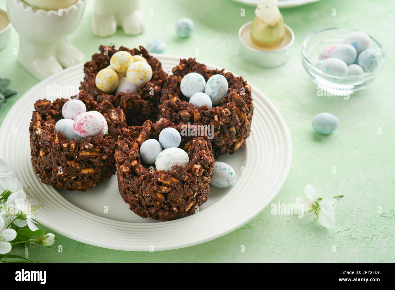 Osterschokolade-Nestkuchen mit Mini-Schokoladeneiern mit blühenden Kirsch- oder Apfelblüten auf grünem Hintergrundtisch. Kreatives Rezept für Easte Stockfoto