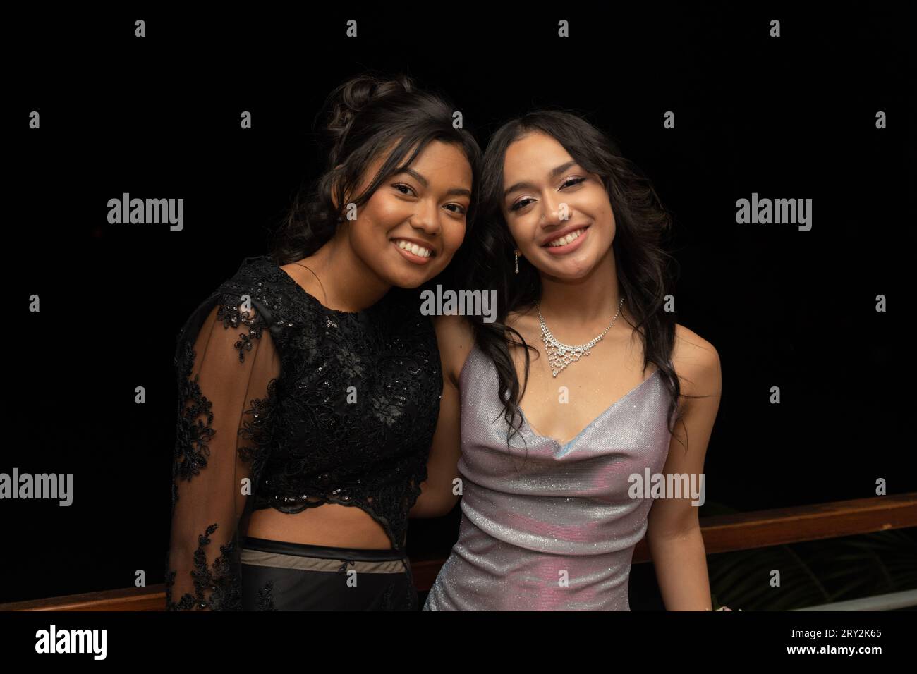 Bei einem Abschlussball aus der Nähe lächeln zwei junge Frauen strahlend in die Kamera und strahlen Freude und Eleganz aus Stockfoto