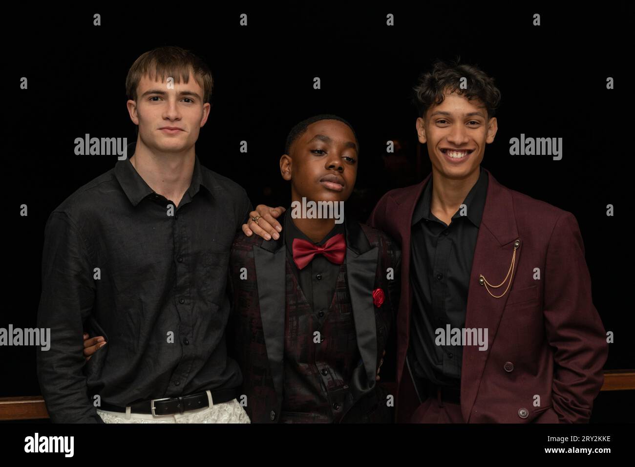 In einer Nahaufnahme versprühen drei stylische, multirassische junge Männer auf dem Abschlussball Selbstvertrauen und Kameradschaft, während sie in eine Pose gehen Stockfoto