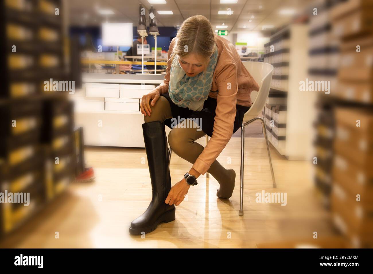 Symbolbild: Elegante junge Frau, die kniehohe schwarze Stiefel in einem Geschäft anprobiert (Modell veröffentlicht) Stockfoto