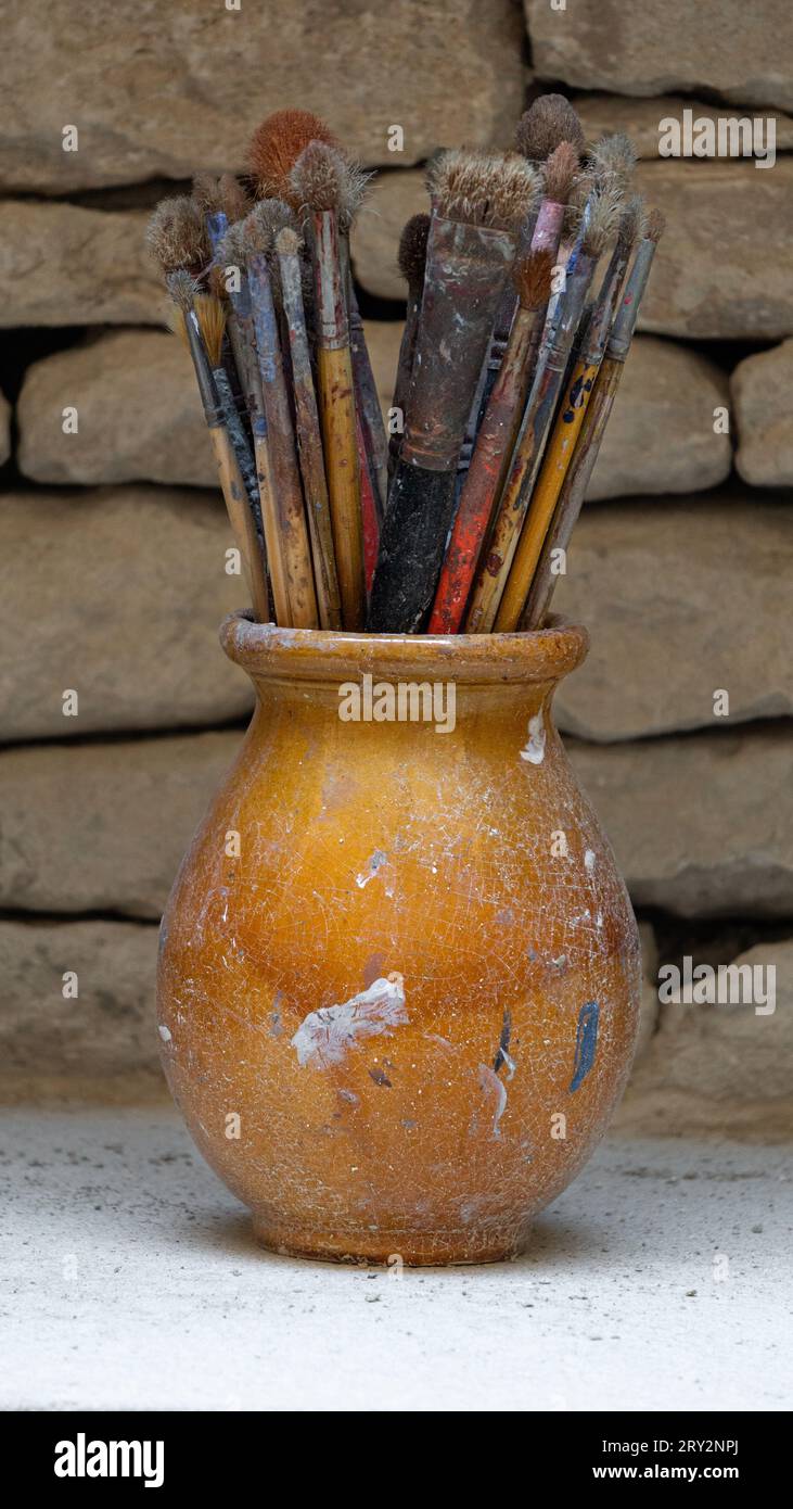 Eine Schüssel voller alter und abgenutzter Pinsel mit Farbflecken darauf. Stockfoto
