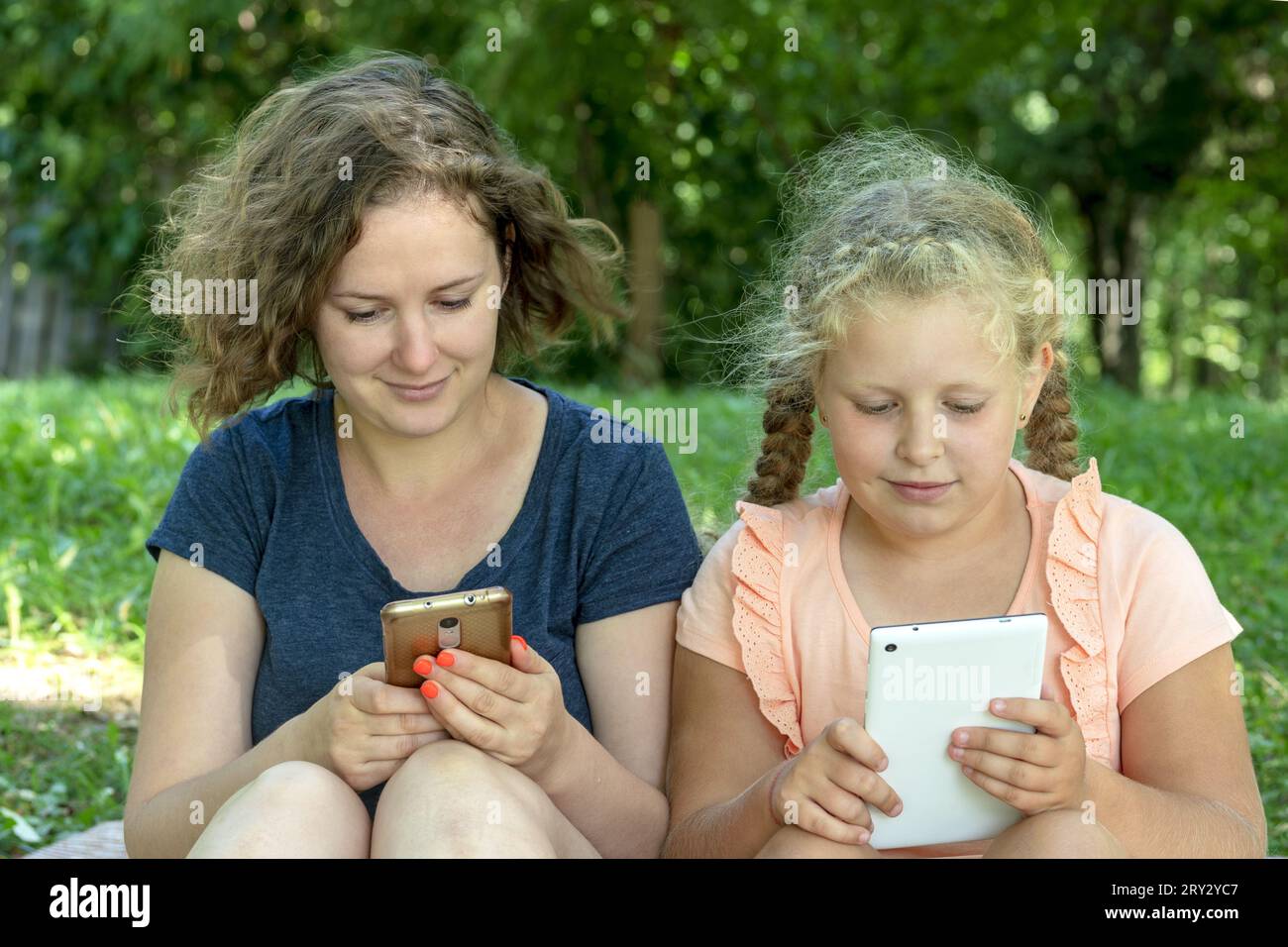 Mutter und Tochter mit Gadgets. Die Frau und das Kind halten das Smartphone, Tablets. Das Konzept Freizeit für Familien auf Picknick. Mangelnde Kommunikation Stockfoto