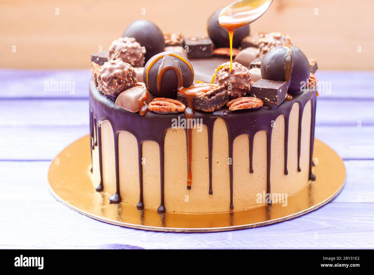 Nahaufnahme der Frau, die gesalzene Karamellsauce auf den Schokoladenkuchen gießt, dekoriert mit Süßigkeiten, Trüffeln, Keksen und Nüssen Stockfoto