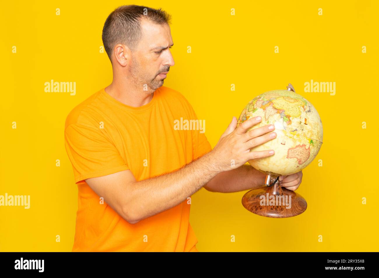 Hispanischer Mann mit Bart in seinen 40ern auf der Suche nach einem Ort auf einer Weltkugel, isoliert auf gelbem Hintergrund. Stockfoto