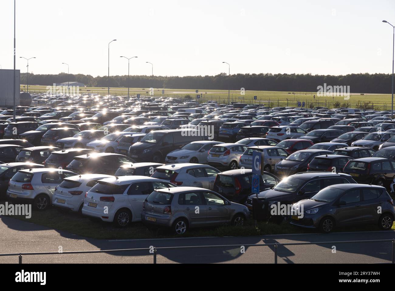 Flughafenparkplatz P5 am Flughafen Eindhoven, Niederlande, mit vielen geparkten Autos, die in der Sonne glitzern, in der Nähe der Landebahn Stockfoto