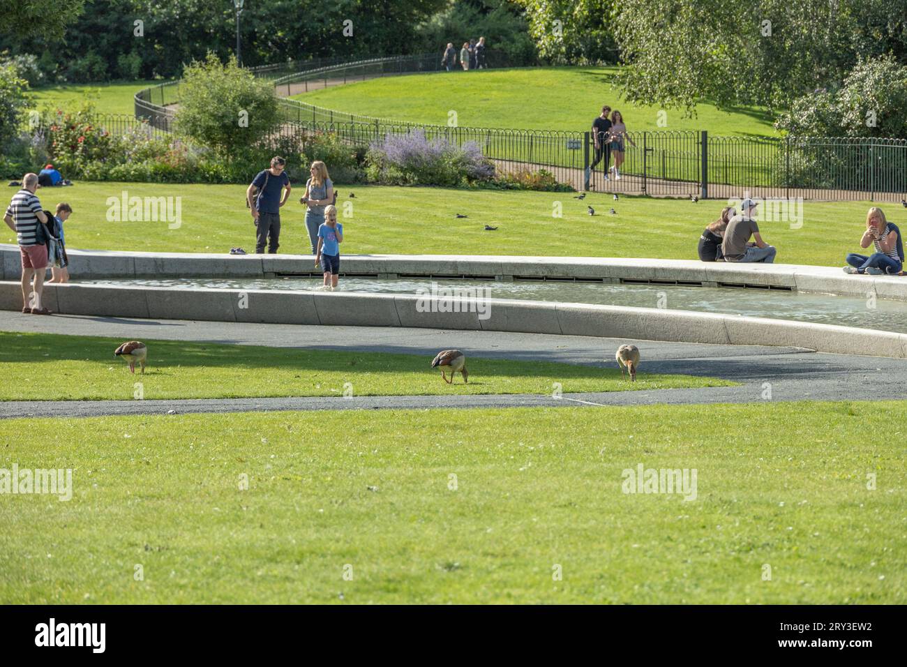 Sonniger Tag in London am Princess Diana Memorial Fountain mit Familien und Paaren, die den Brunnen genießen und durch den Hyde Park spazieren gehen. Stockfoto