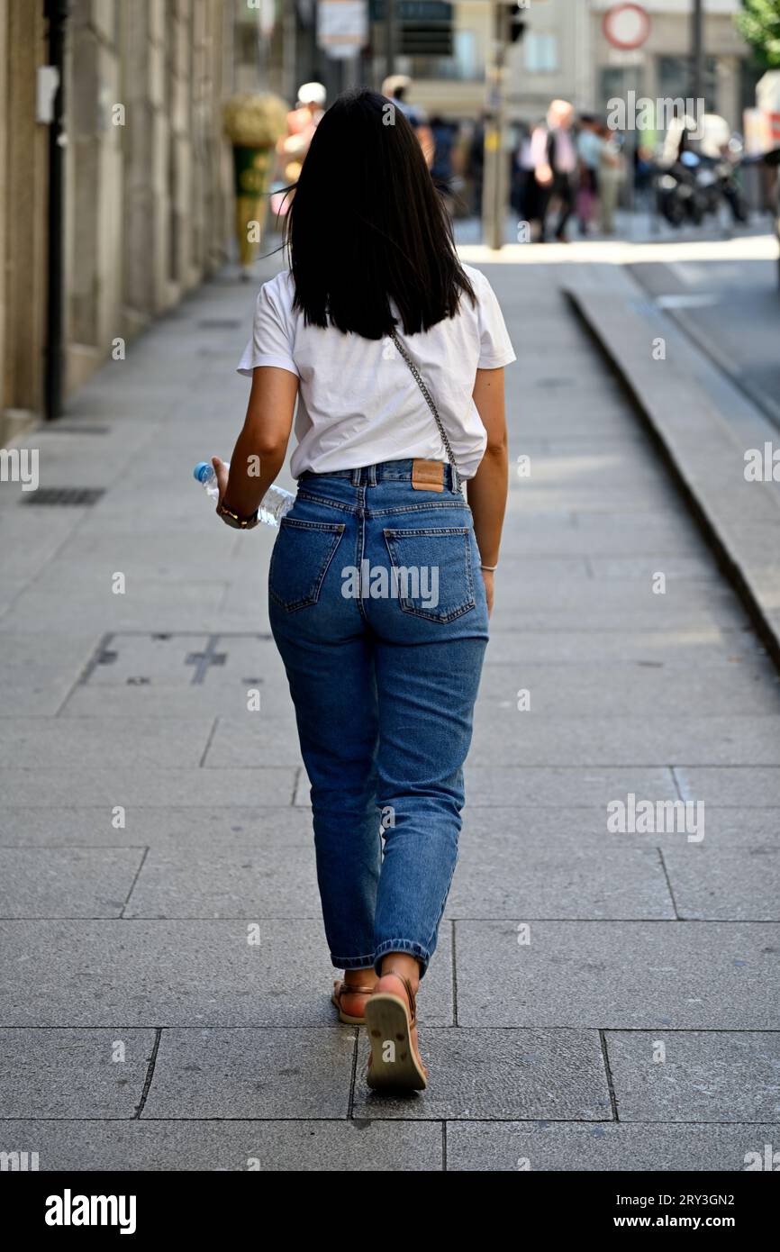 Rücken einer jungen erwachsenen Frau, die Jeans trägt, die auf dem Bürgersteig weggeht Stockfoto