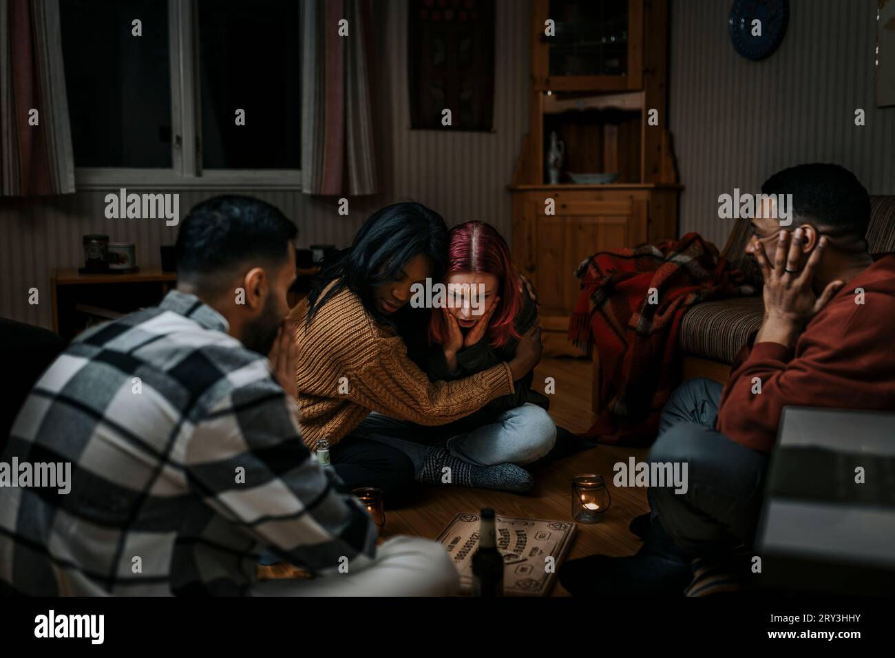 Verängstigte multirassische Freunde mit Ouija-Board in einer Spukkabine Stockfoto